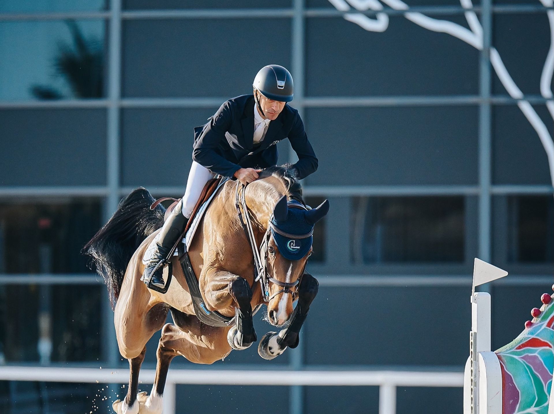 Equestrian rider in helmet jumping over obstacle on a horse during competition.